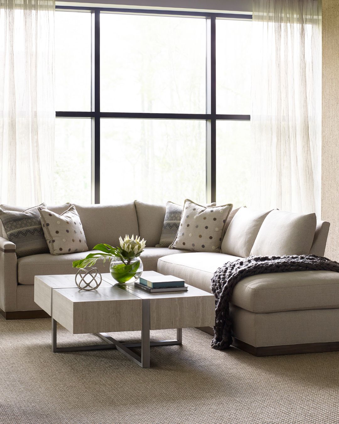 Modern living room with a beige sectional sofa, coffee table, and large windows.