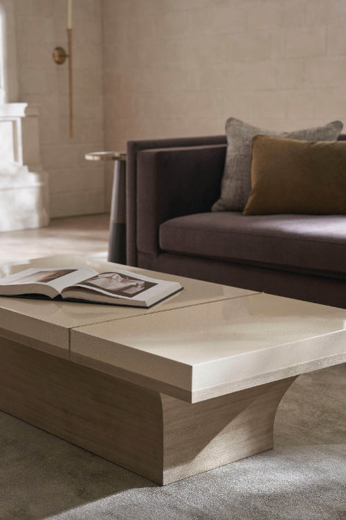 Close-up of cream lacquer coffee table with wood base beside brown velvet sofa