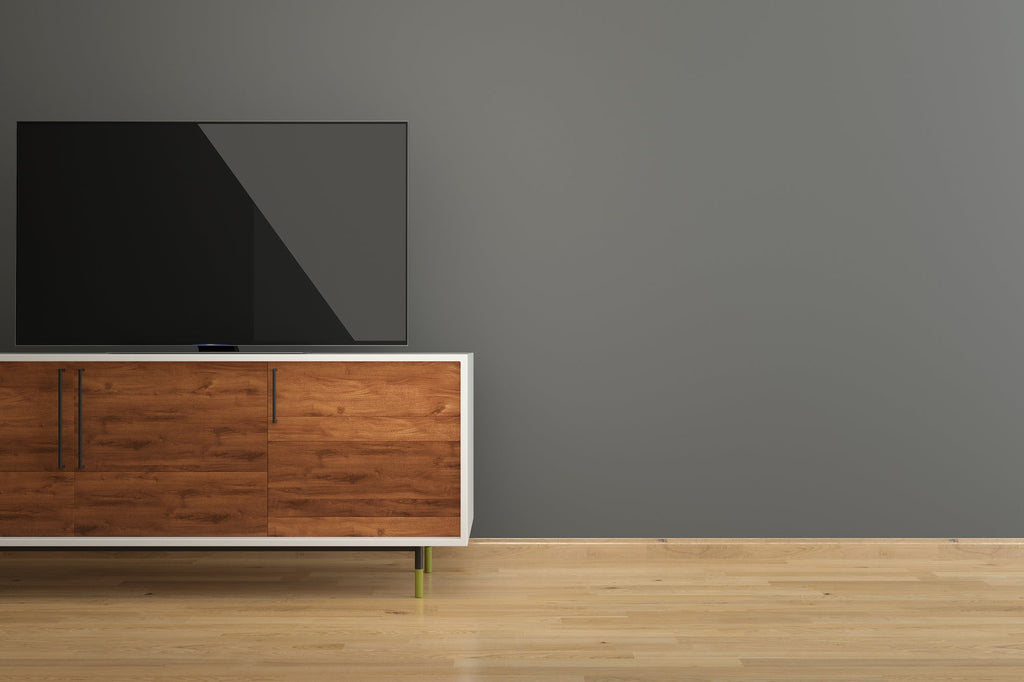 Flat-screen TV sitting on a mid-century style TV stand with walnut wood panel doors, a white frame, and slim coloured legs against a grey wall