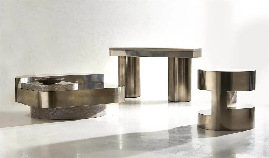  Collection of three sculptural brushed bronze metal tables — low oval coffee table, square dining height table on cylinder legs, and C-shaped accent side table