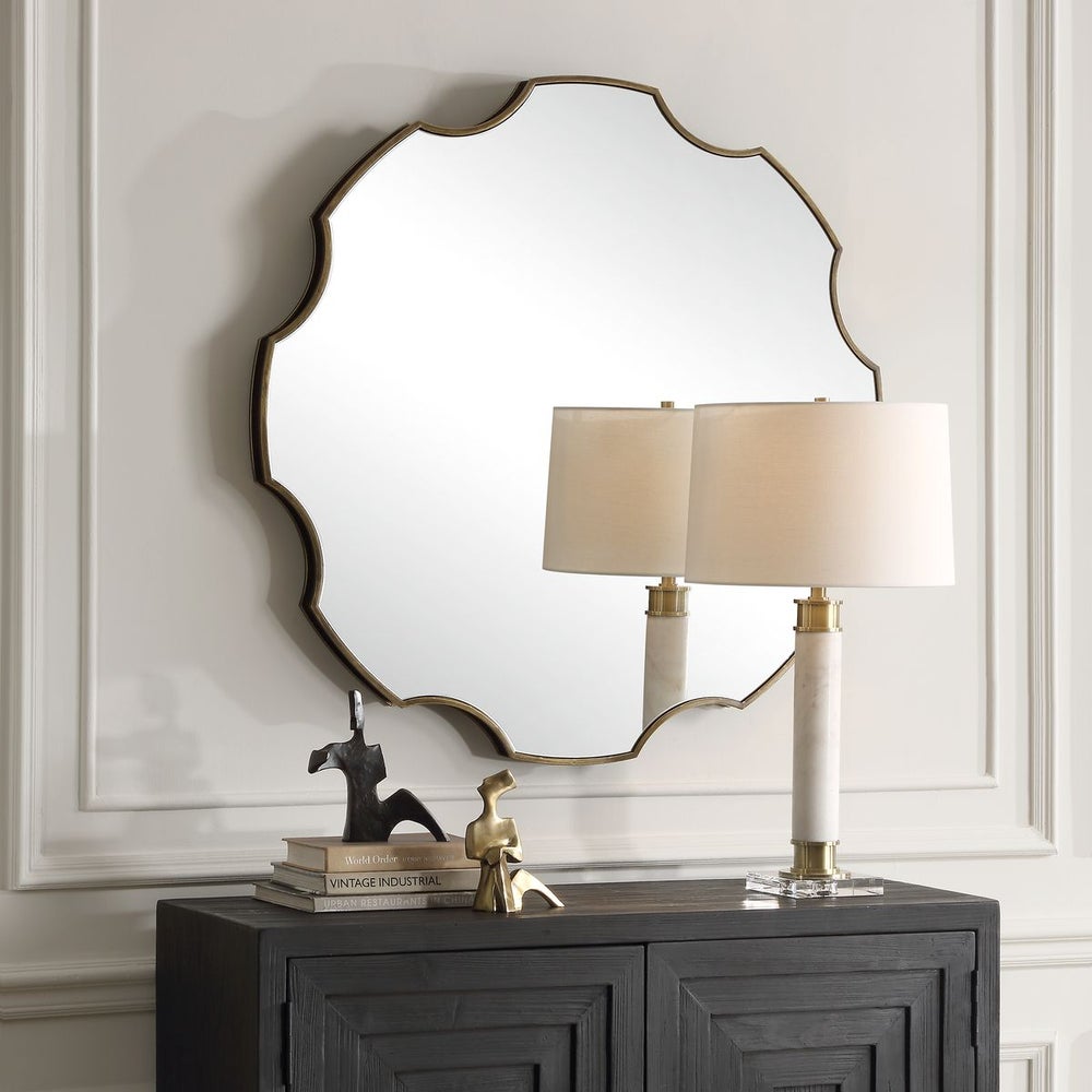 Large scalloped edge wall mirror with antique gold frame above black two-door console cabinet with marble and brass table lamp