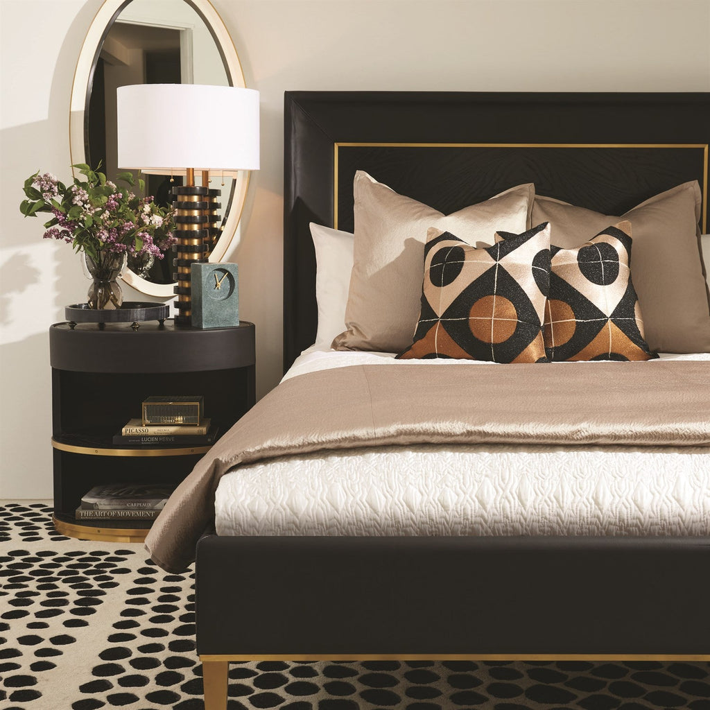 Black upholstered bed with gold trim panel headboard and brass legs styled with geometric throw pillows in Art Deco bedroom