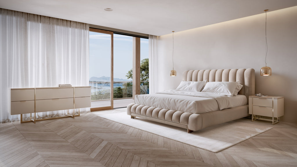 Beige channel-tufted upholstered bed with tufted footboard and matching brass nightstand and six-drawer dresser in minimalist bedroom with ocean view