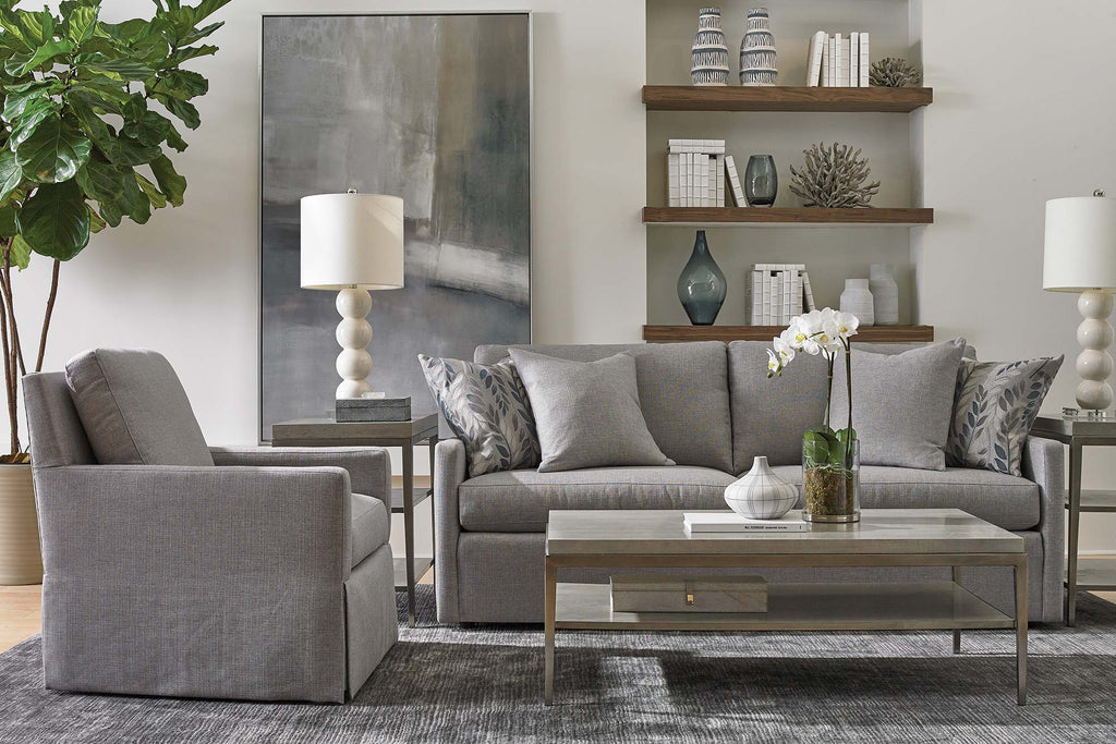 Gray upholstered sofa and swivel accent chair with leaf-print pillows, marble coffee table, and walnut floating shelves in a transitional living room