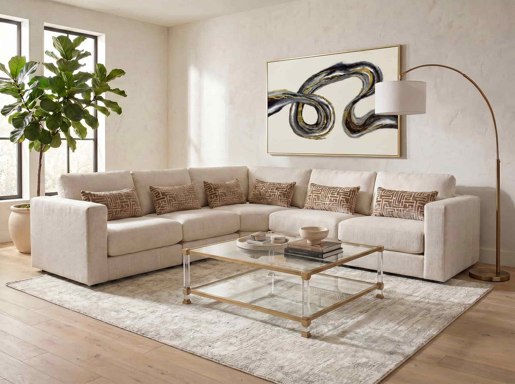 Neutral living room with large L-shaped cream sectional sofa, geometric patterned lumbar pillows, acrylic and brass glass coffee table, and arc floor lamp