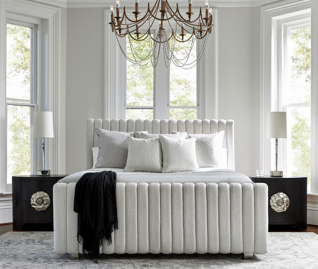 White channel-tufted upholstered bed with tall wingback headboard and footboard in elegant bedroom with chandelier and dark wood nightstands
