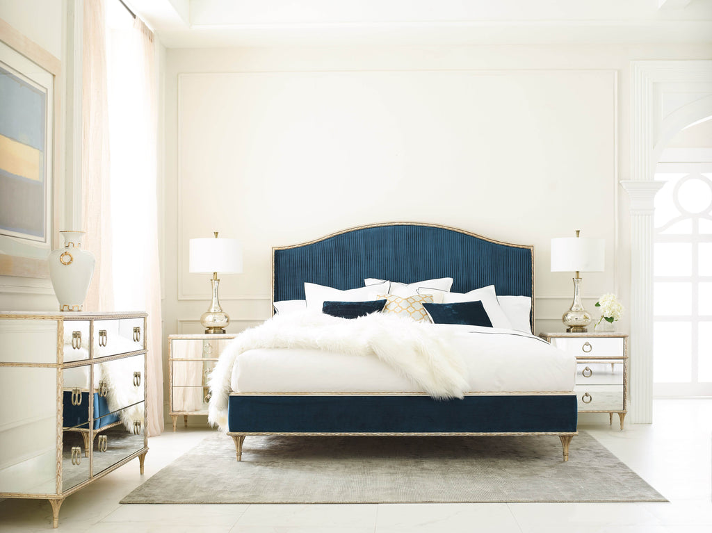 Navy velvet upholstered bed with mirrored bedroom set in a light, glamorous bedroom featuring gold accents and faux fur throw.