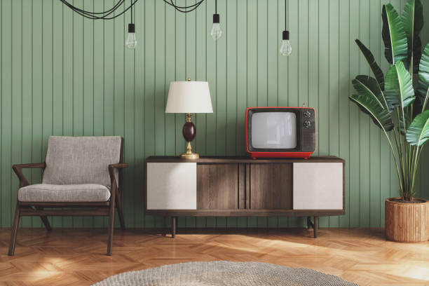 Retro mid-century living room with walnut cane-front dresser, vintage radio, green ceramic lamp, and grey armchair against sage green textured wall.