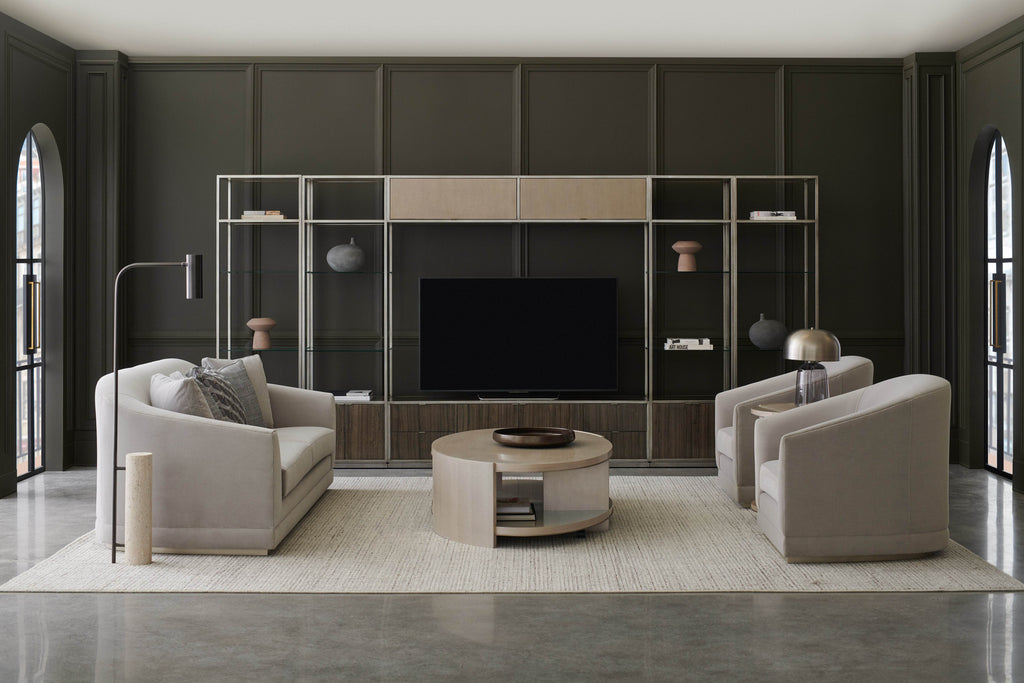 Contemporary living room with two upholstered armchairs and a round coffee table facing a media wall with open shelving and a dark paneled backdrop.