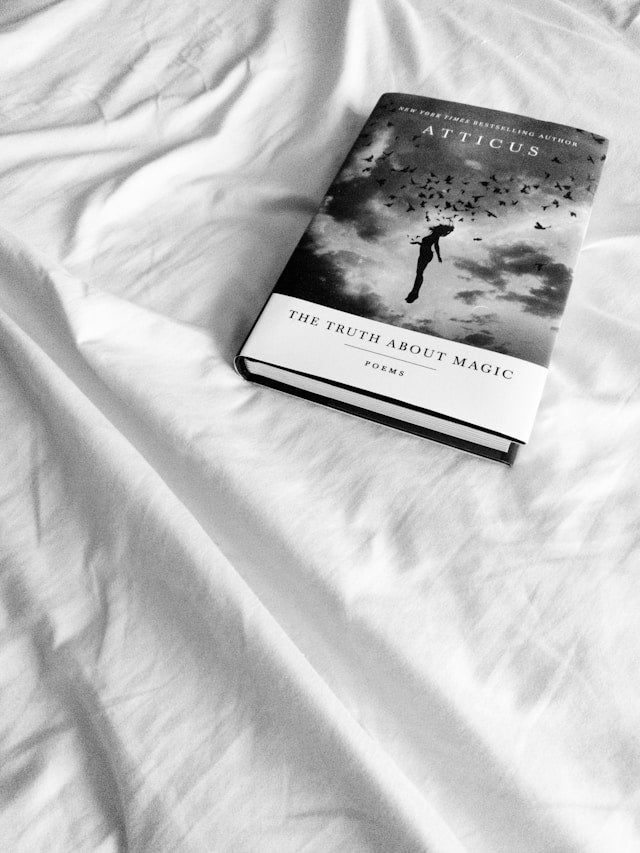  Book "The Truth About Magic" by Atticus lying on white bed sheets.