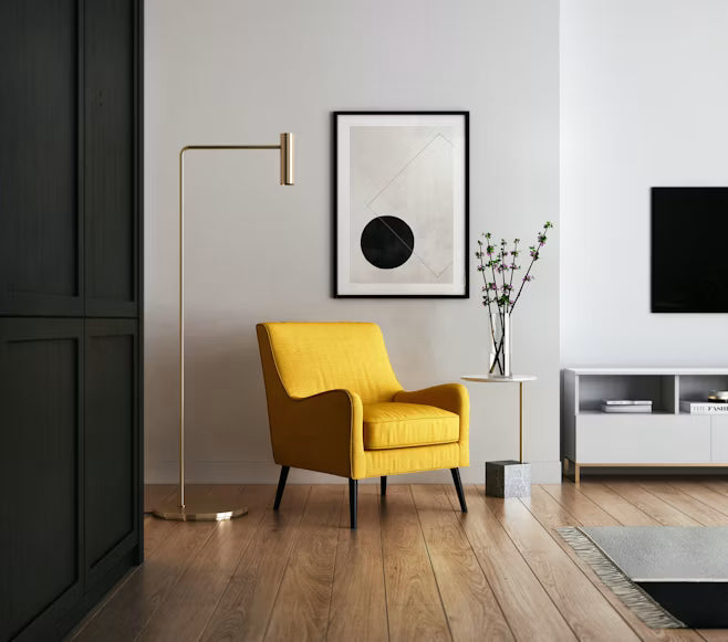 Yellow accent armchair with black legs beside a brass floor lamp in a minimalist modern living room with light wood floors and white walls.