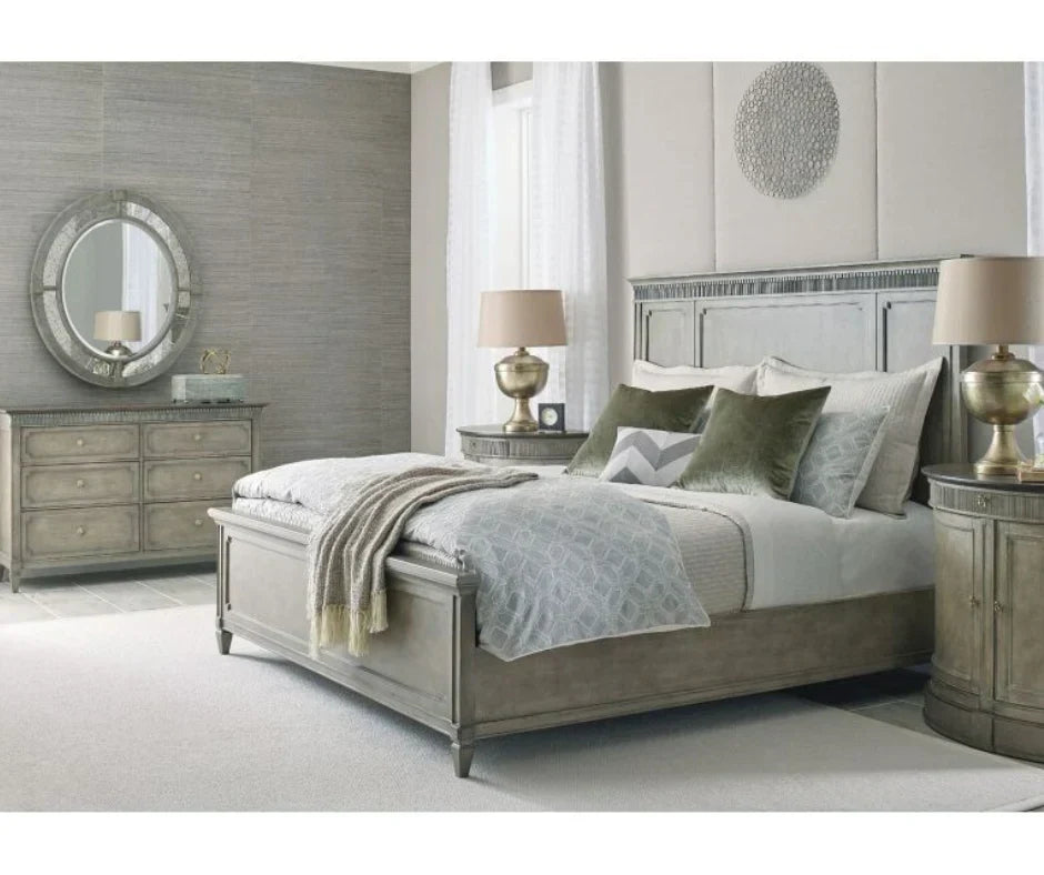 Transitional grey bedroom set with panel bed, six-drawer dresser, round antiqued mirror, curved nightstands, and gold urn table lamps with sage green accent pillows