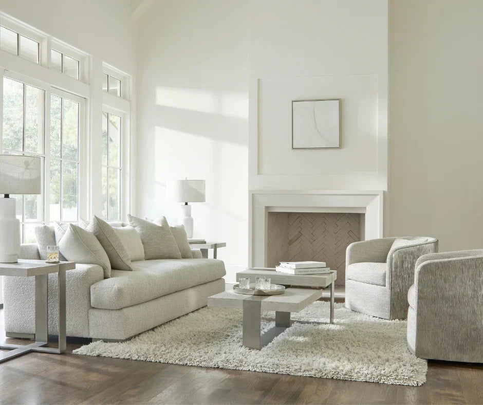  Bright minimalist living room with cream bouclé sofa, swivel accent chairs, stone coffee table, shag rug, and white fireplace surround