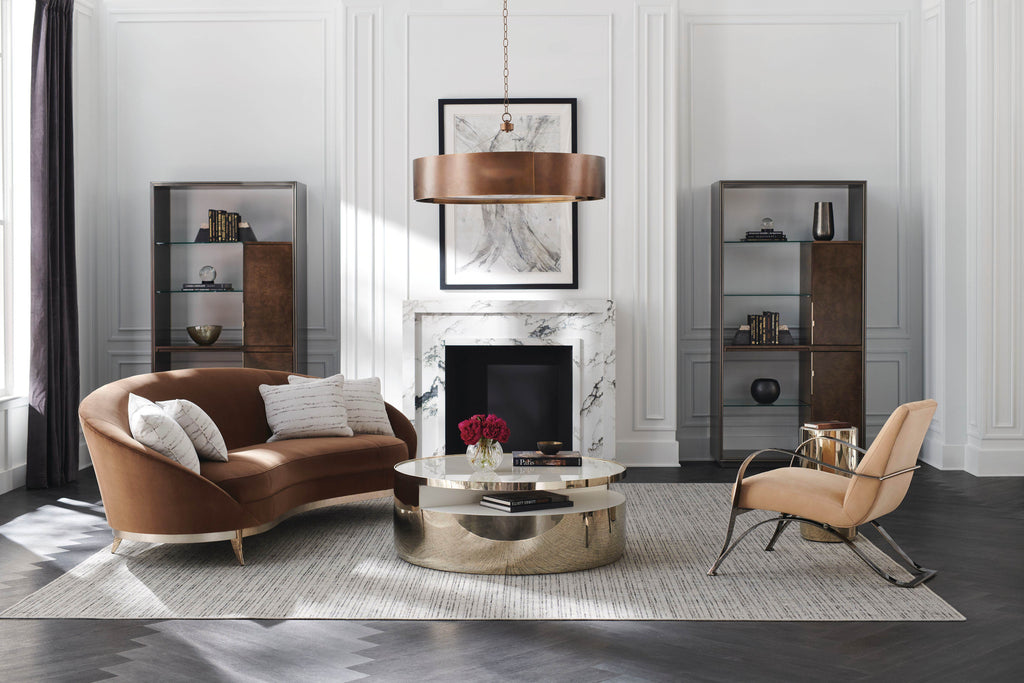 Elegant living room with curved sofa, sculptural armchair, round cocktail table, and brass chandelier set before marble fireplace and glass cabinets.