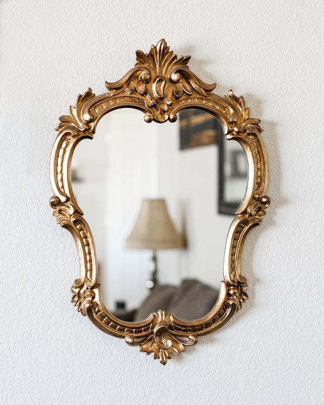 Ornate gold baroque wall mirror with decorative carved frame and floral scrollwork.