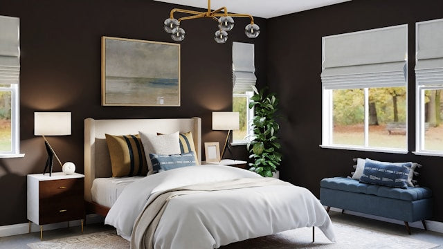 Dark moody bedroom with cream upholstered bed, gold pendant light, mustard and blue accent pillows, and dark brown walls.