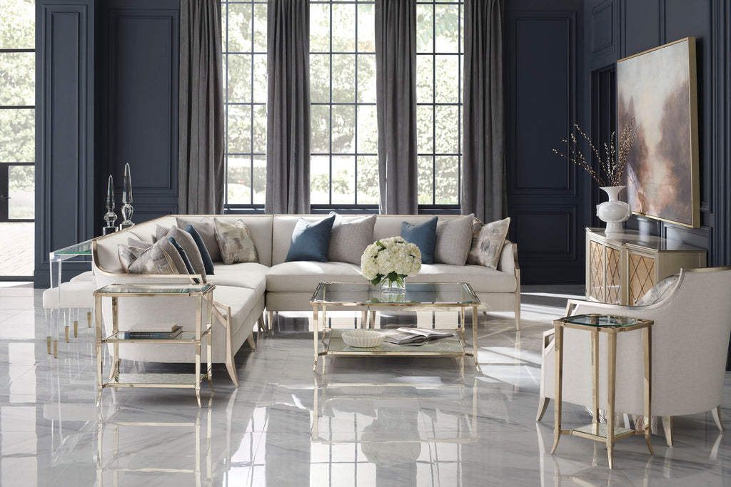 Luxury cream upholstered L-shaped sectional sofa with gold metal legs and glass coffee table in elegant navy blue living room