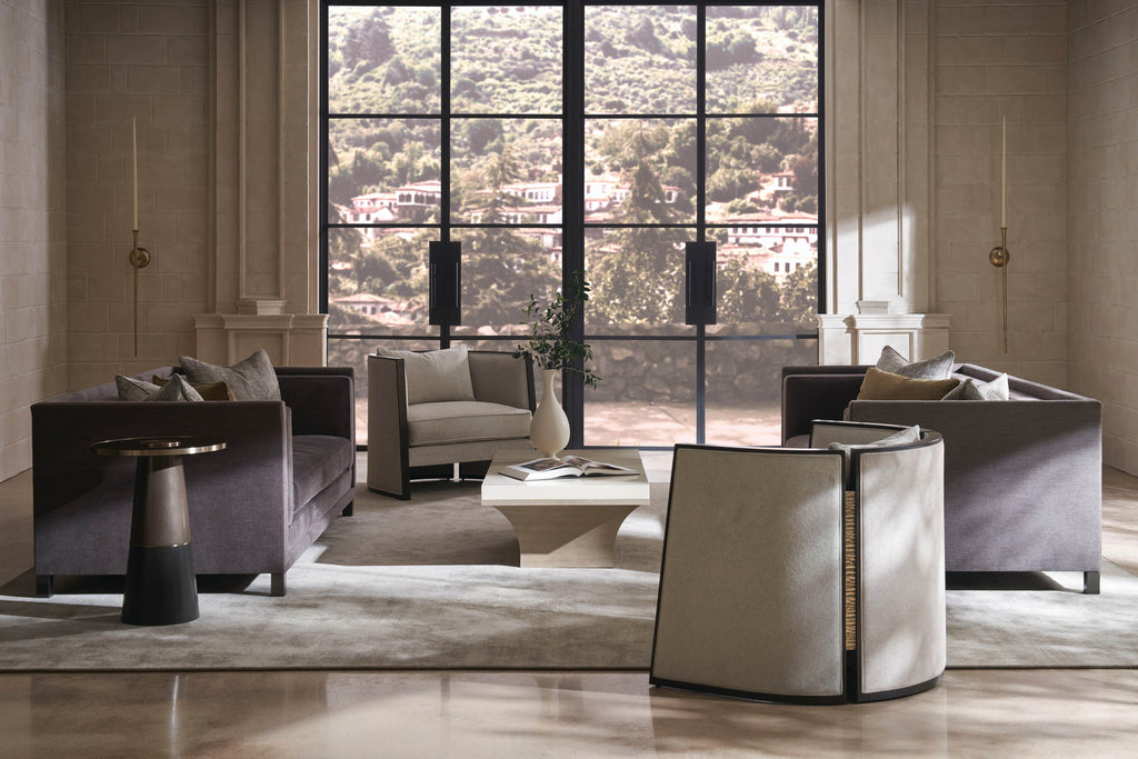 Modern luxury living room with charcoal velvet sofas, cream barrel accent chair, sculptural side table, and travertine coffee table in a high-ceiling space with steel-frame windows