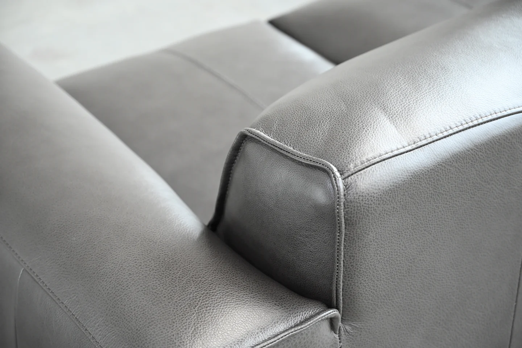 Close-up of grey leather sofa armrest showing premium leather texture and stitching detail.