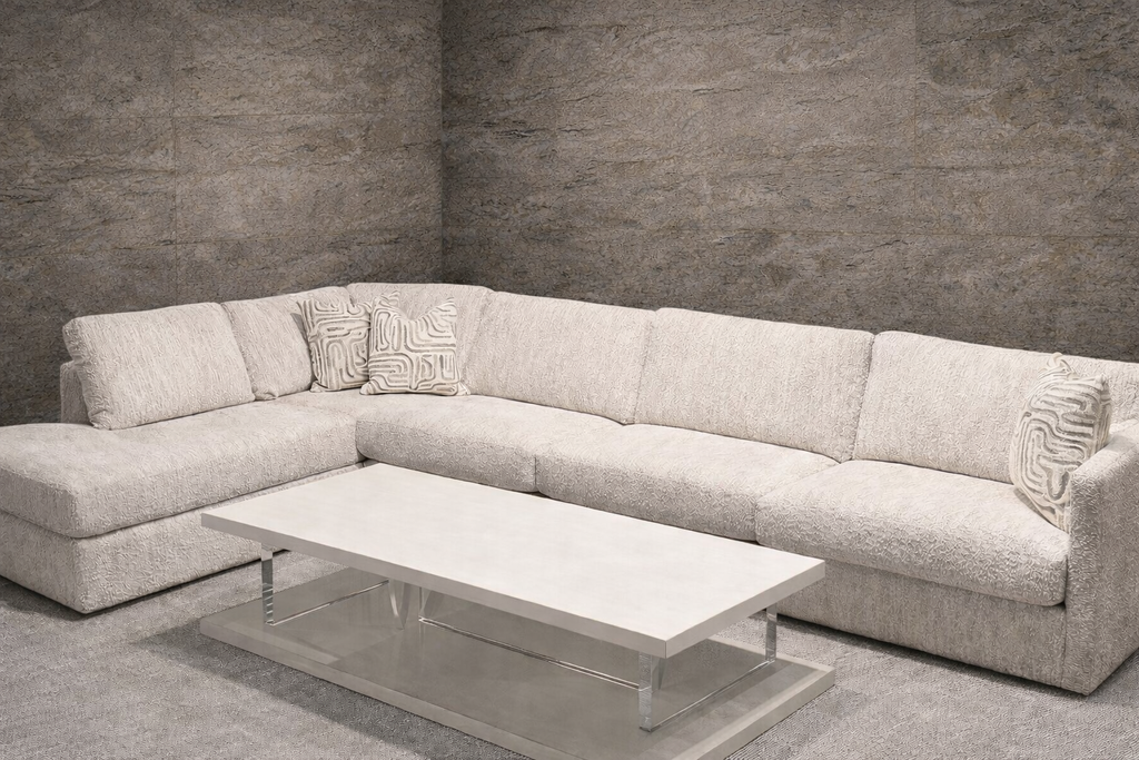 Large cream textured fabric L-shaped sectional sofa with decorative pillows and chrome coffee table.