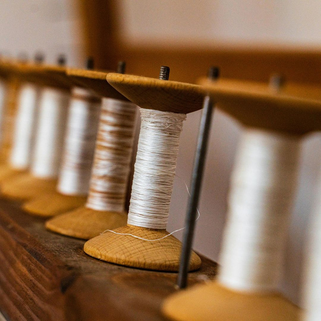 Spools of white thread on wooden spindles against a neutral background