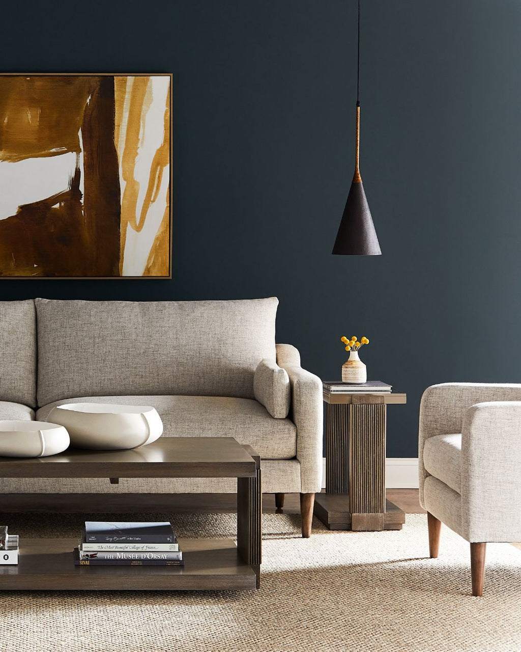 Modern living room with gray sofa, armchair, and abstract art on a dark wall.