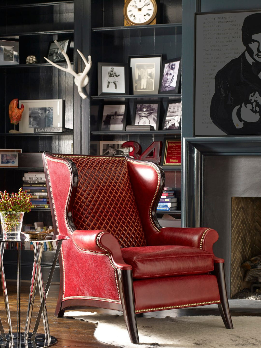 A red leather wingback armchair with diamond-patterned back upholstery and dark wood legs, styled in a dark, elegant room with bookshelves and a fireplace.