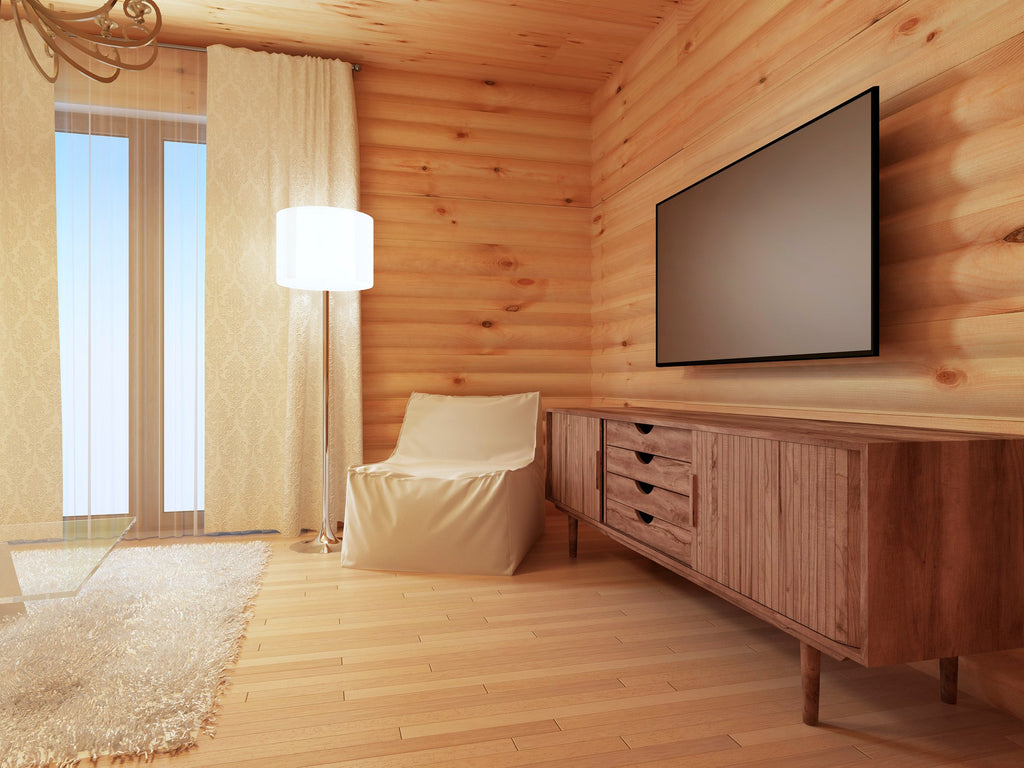 Walnut wood TV credenza with fluted drawer fronts styled in a warm log-cabin living room with a wall-mounted TV and accent chair.
