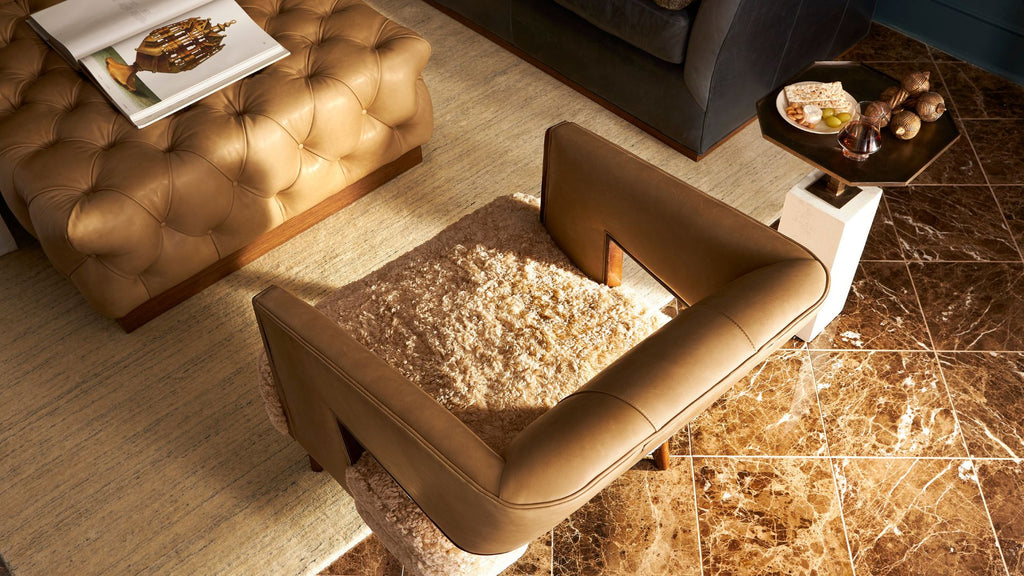 A modern brown leather armchair with a textured beige shag rug on its seat, styled in a contemporary living room next to a tufted ottoman and marble tile flooring.