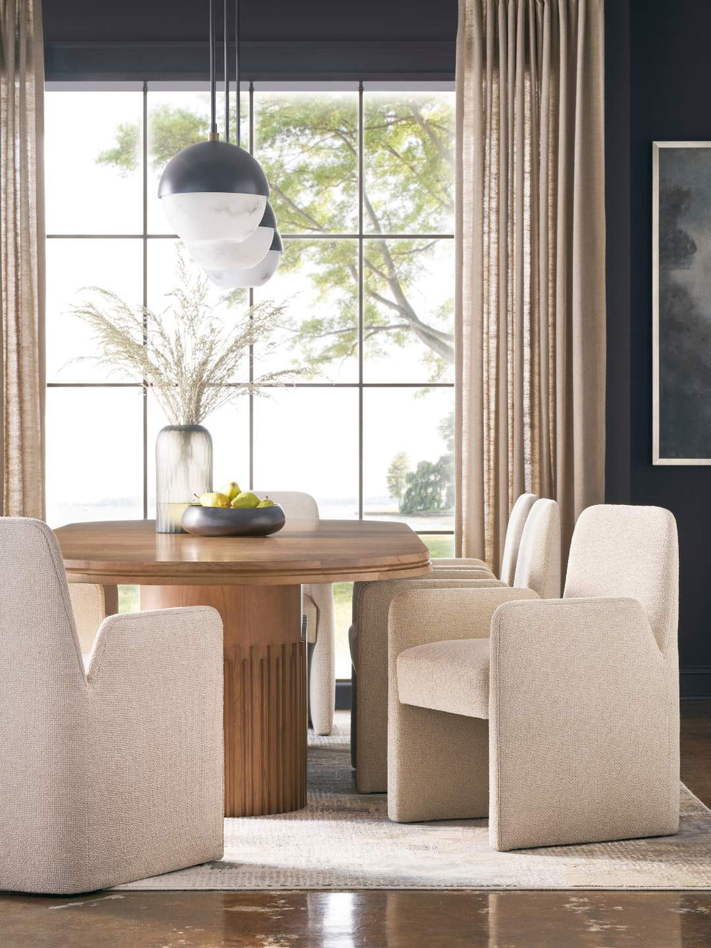 Quiet luxury oval dining table with fully upholstered dining armchairs.