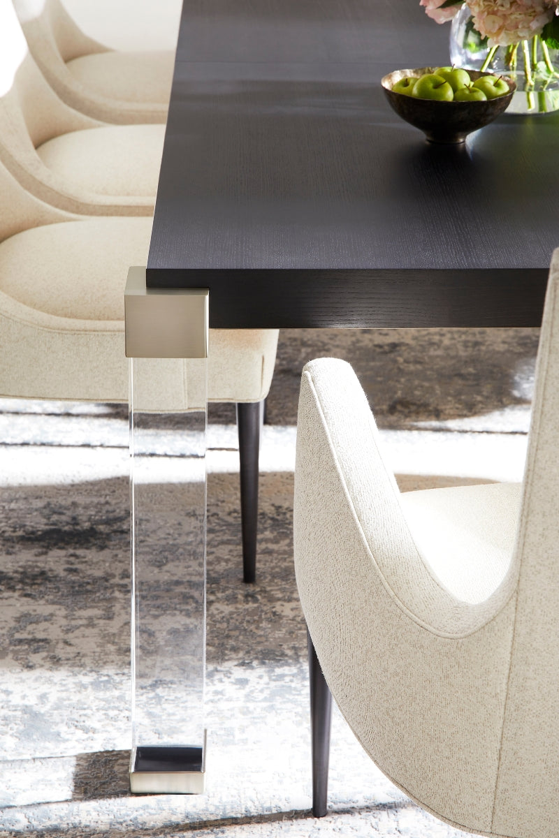 Modern dining table with dark wood surface and acrylic legs in a room with chairs and decor.