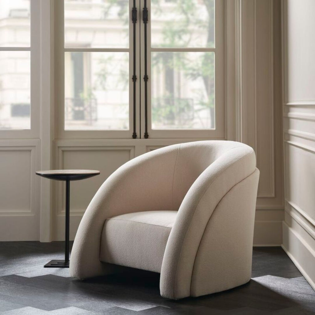 Beige armchair in a room with large windows and a small round table.