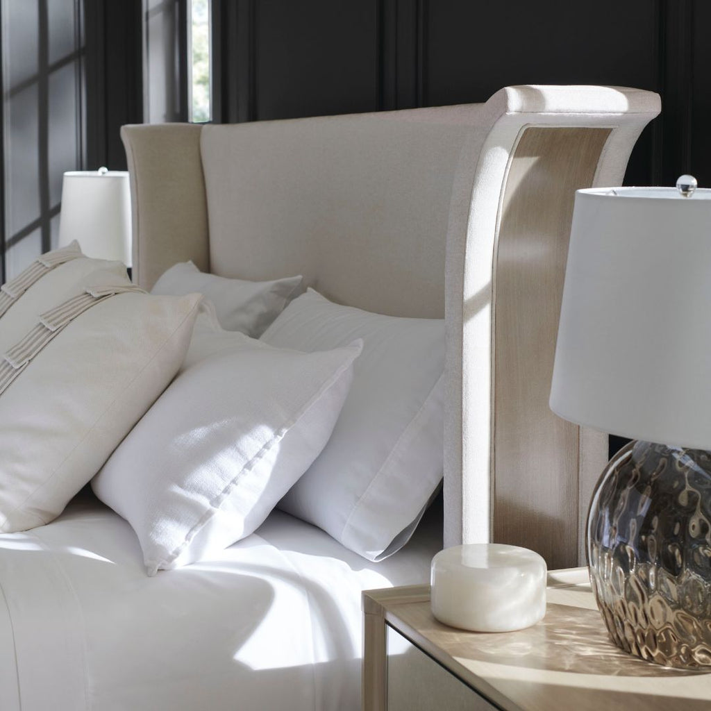 Neatly made bed with white pillows and a lamp on a nightstand in a bedroom setting.