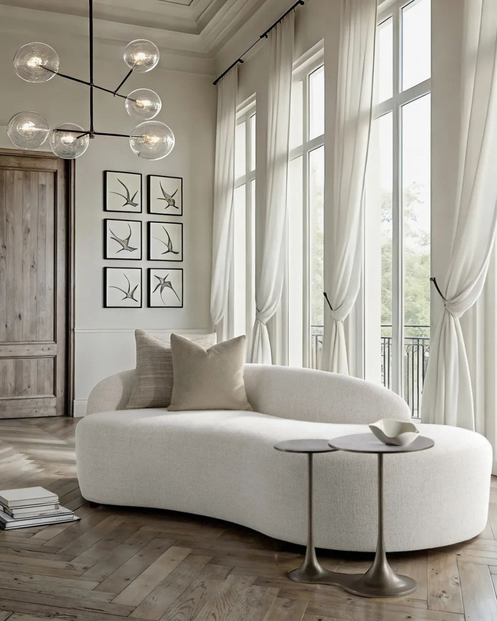 Modern living room with a white sofa, stylish chandelier, and large windows.