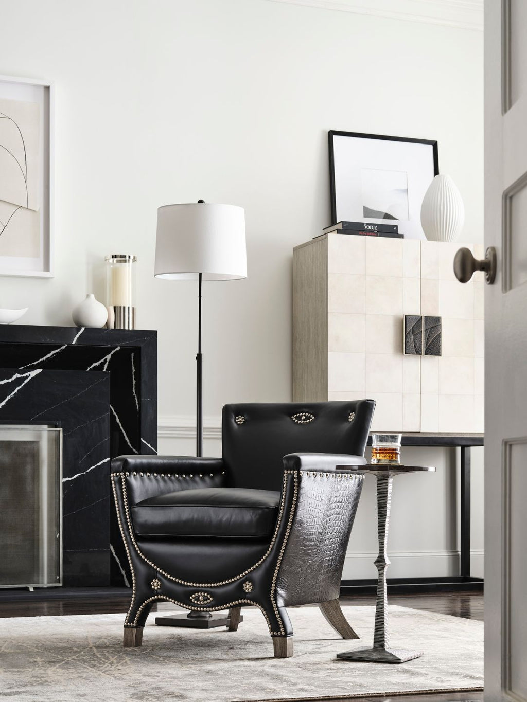 A black leather armchair with gold nailhead trim and a textured gray side table in a modern, elegantly styled living room.