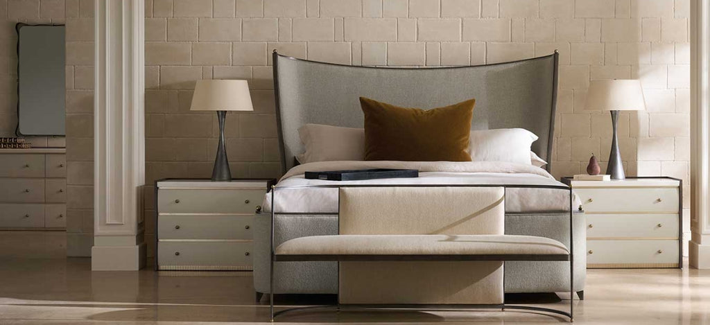 A modern bedroom featuring a bed with a tall upholstered headboard, white bedding, a mustard yellow accent pillow, a matching bench at the foot of the bed, and two bedside nightstands with lamps.