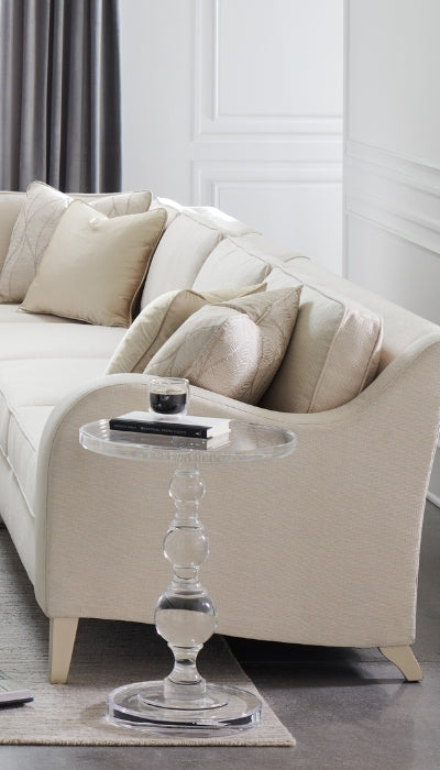 Beige sectional sofa with decorative pillows and a glass side table in a living room setting.