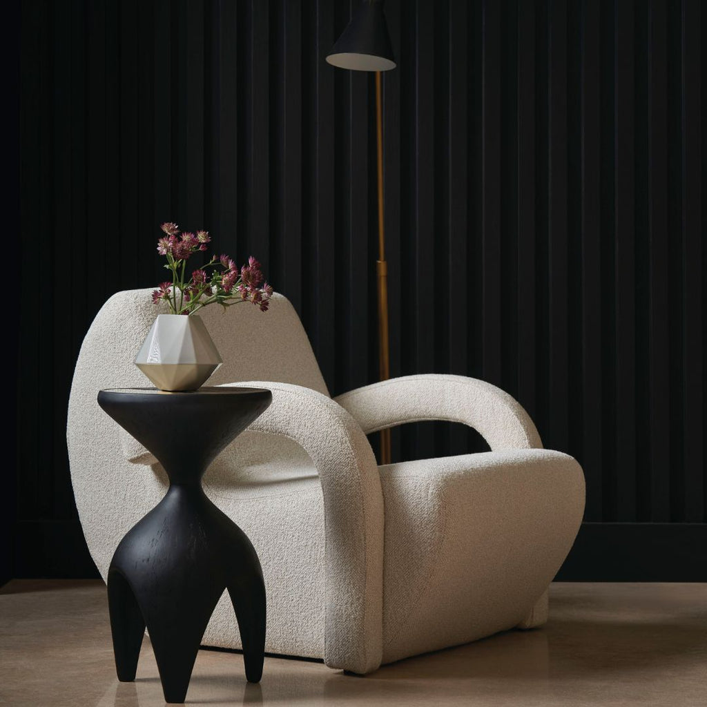 Modern beige armchair with a black side table and geometric vase against a dark curtain background