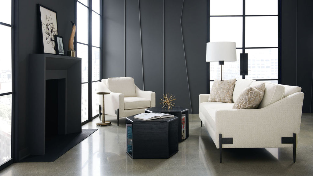 A modern living room interior featuring a white sofa with beige pillows, a matching white armchair, a black fireplace, and a black coffee table on a polished concrete floor.