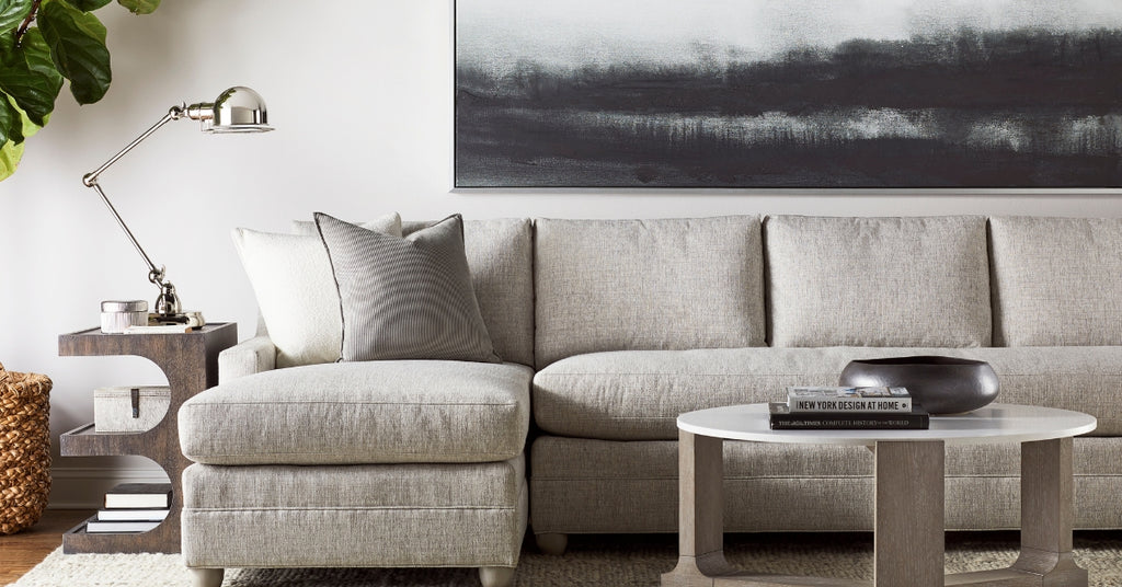 Modern living room with a gray sectional sofa, round coffee table, and abstract painting on the wall.