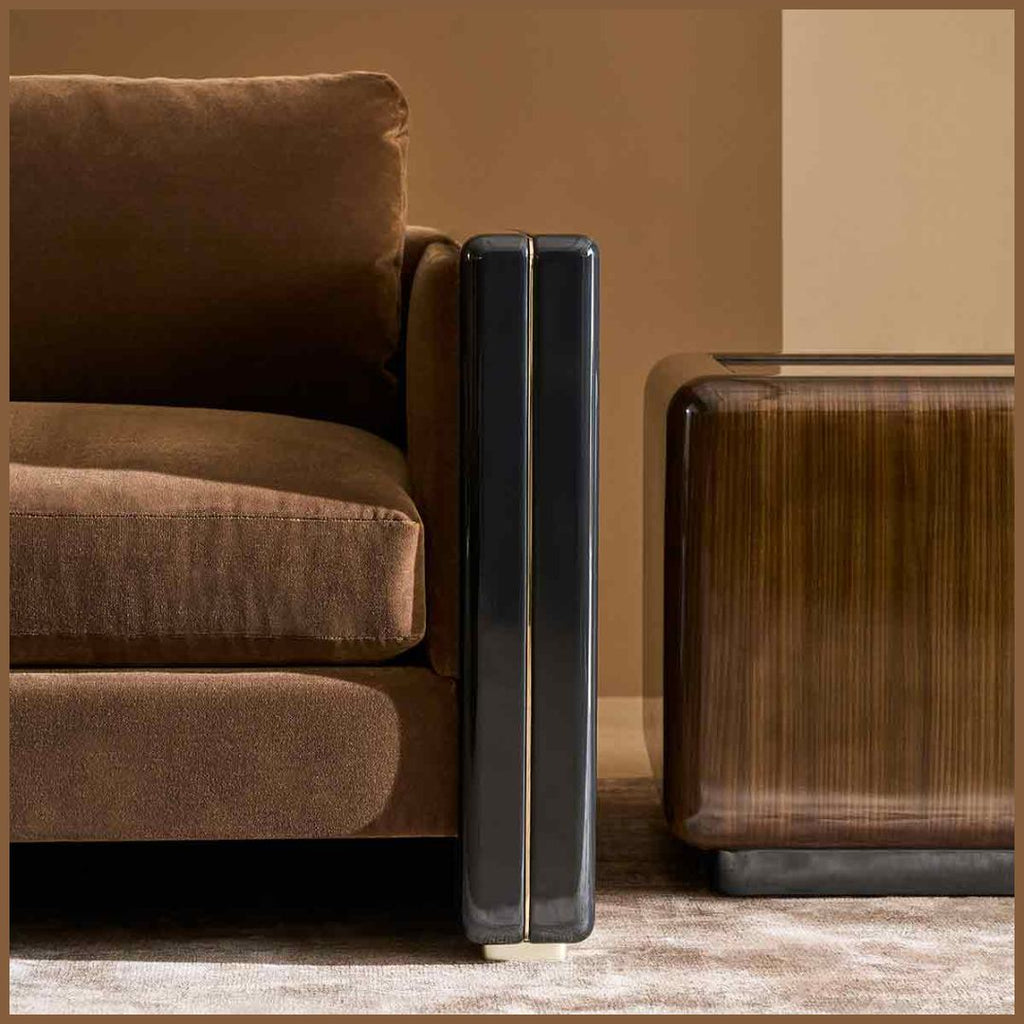A close-up of a brown upholstered sofa beside a dark wood side table, with a glossy black rectangular object standing between them on a light rug against a warm brown wall.