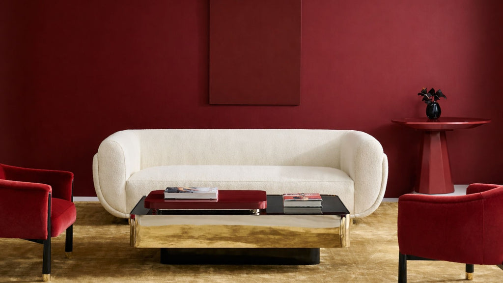 Modern living room with a white sofa, red chairs, and a coffee table against a red wall.