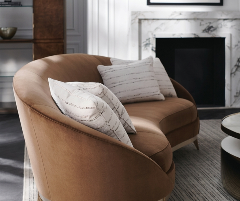  Curved caramel leather armchair with a rounded back and a soft cushion, placed in a dimly lit living room beside a dark, textured wall