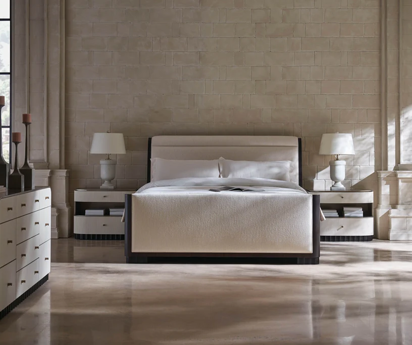 Upholstered bed with a tall padded headboard flanked by two matching nightstands and table lamps in a bright, neutral bedroom