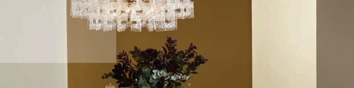 Crystal chandelier with glass drops hanging in a softly blurred, cream colored room, lit with a warm, gentle glow from overhead 