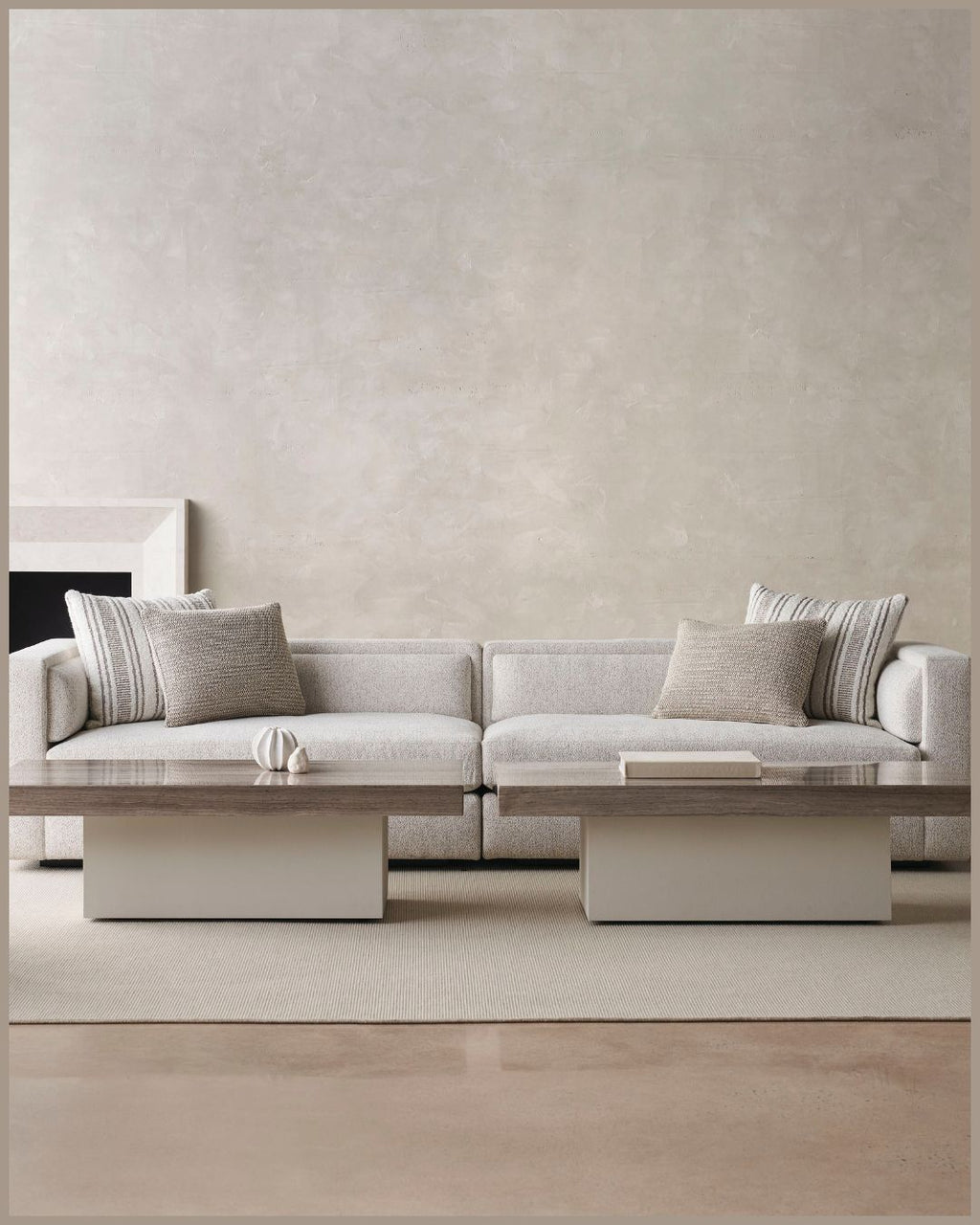 A modern light beige sectional sofa with textured throw pillows, styled in a minimalist living room with a matching low wooden coffee table and a textured beige wall background.