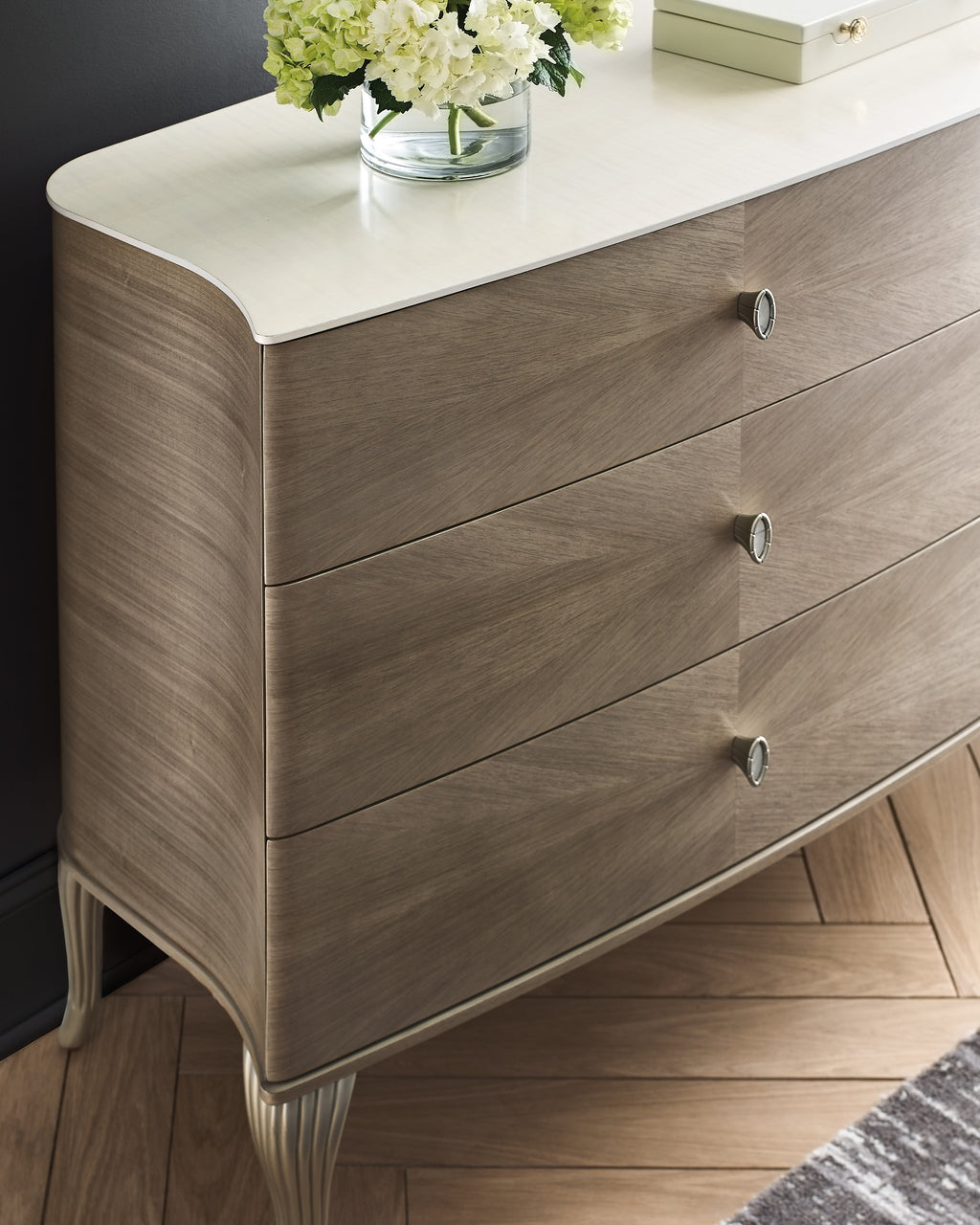 Détail en gros plan d'une commode galbée à trois tiroirs en placage de chêne gris avec plateau en laque blanche et quincaillerie ronde en étain sur pieds galbés