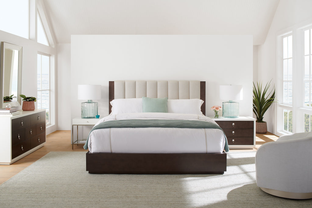 Lit plateforme en noyer foncé avec tête de lit haute capitonnée verticalement et tables de chevet bicolores blanc et bois dans une chambre côtière lumineuse