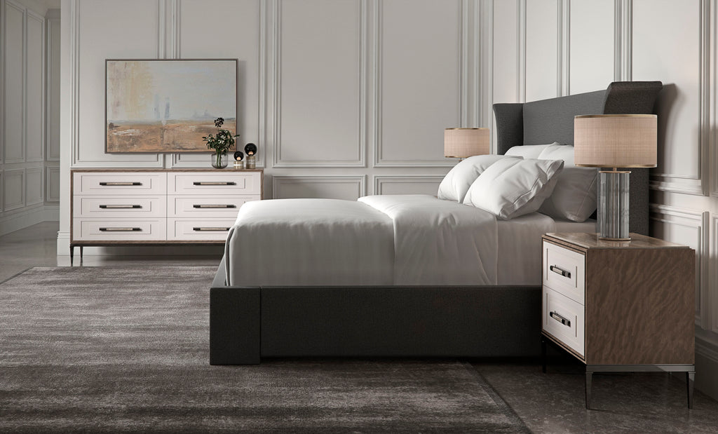 Lit à dossier capitonné en tissu anthracite avec table de nuit bicolore blanc et noyer assortie et commode à six tiroirs dans une chambre lambrissée blanche.