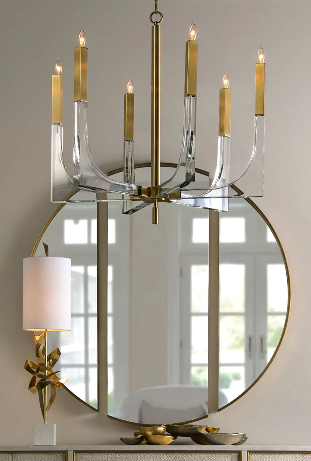 Grand miroir mural rond sans cadre avec fin anneau en laiton, associé à un lustre à huit bras en cristal et laiton au-dessus de la console.